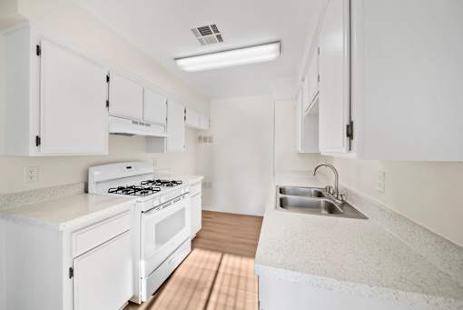 A white kitchen with a stove, sink, and cabinets.