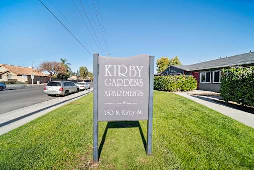 A sign for Kidby Gardens Apartments stands in the grass by a road.