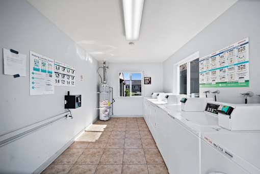 A clean, white-walled room with a tiled floor and a row of sinks on the right side.
