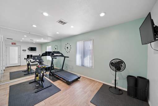 A room with a treadmill, exercise bike, and a fan.