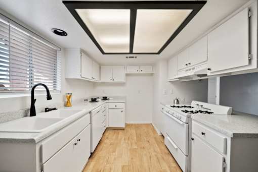 A white kitchen with a black ceiling and wooden floors.