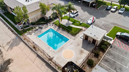 An aerial view of a swimming pool surrounded by a fence and a parking lot.