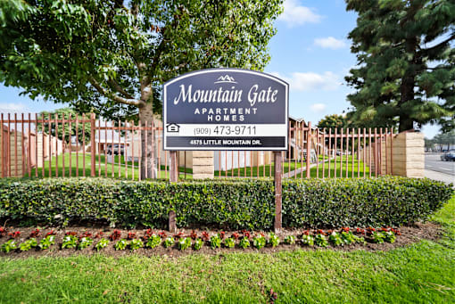 A sign for Mountain Gate Apartment Homes is displayed in front of a fence.