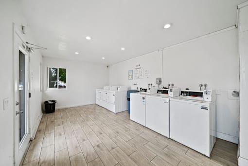 A white room with a wood floor and a white wall with a window.