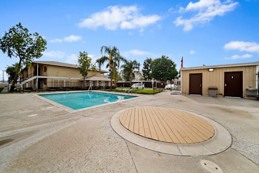 A large outdoor swimming pool with a wooden deck in the middle of a concrete area.