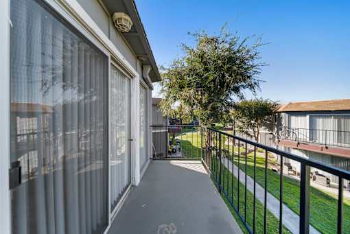 A balcony with a black railing and a tree in the background.