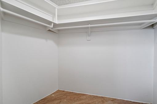 A white room with a wooden floor and a white ceiling with a pipe.