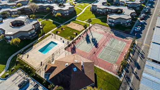 A tennis court is surrounded by a fence and a swimming pool.