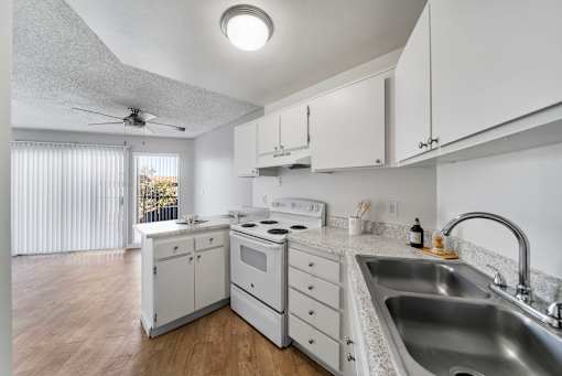 A white kitchen with a stove, sink, and fan.