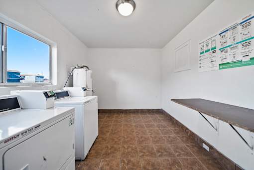 A white washing machine sits in a room with a window and a tiled floor.
