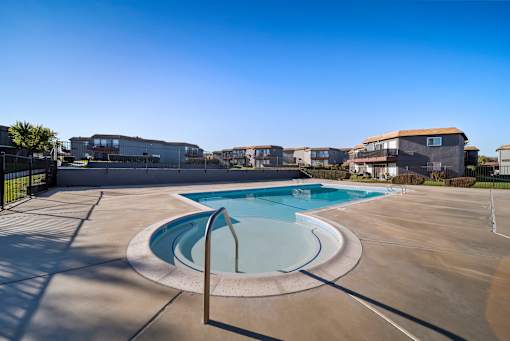 A round swimming pool in the middle of a concrete area with buildings in the background.