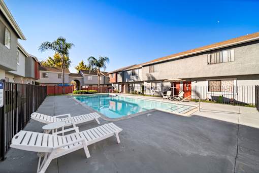 A pool area with sun loungers and a fence.