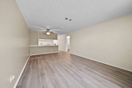 A room with a ceiling fan and light fixture, and a long wooden floor.