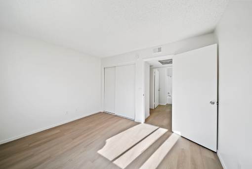 A room with white walls and a wooden floor with a rug in the middle.
