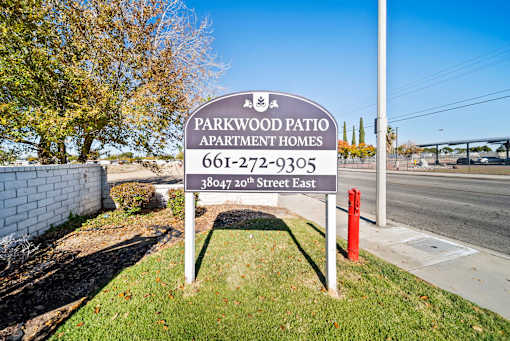 A sign for Parkwood Patio Apartment Homes stands in front of a tree.