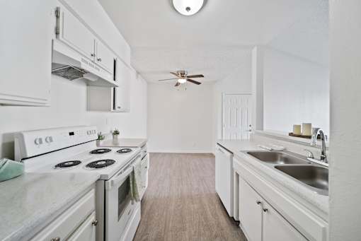 A white kitchen with a stove, sink, and cabinets.