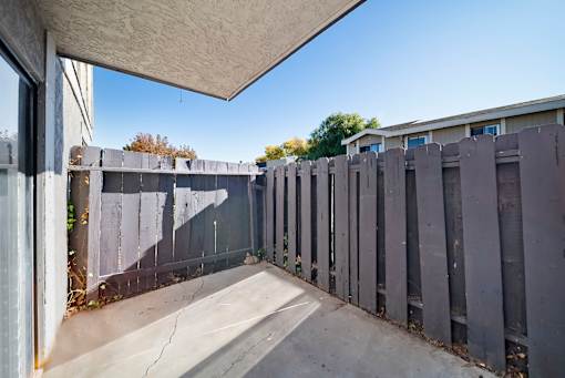 A concrete patio with a grey fence and a white wall.