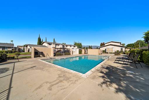 A swimming pool surrounded by a concrete patio and lounge chairs.