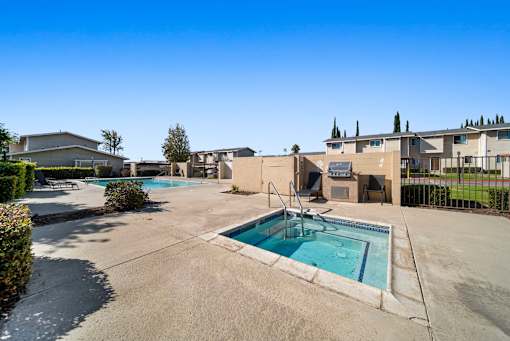 A large outdoor swimming pool surrounded by a concrete patio and buildings.