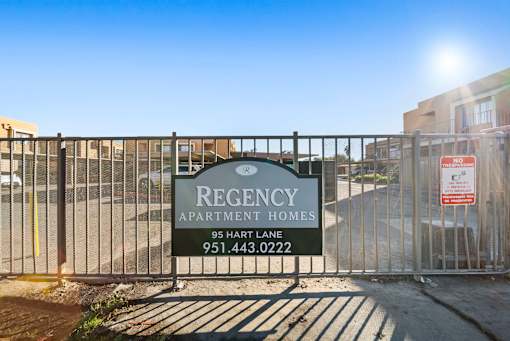 A sign for Regency Apartment Homes is displayed on a fence.