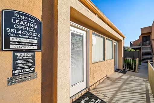A leasing office sign is posted on a wall outside a building.