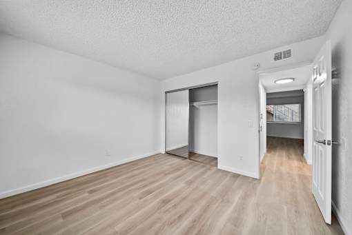 A room with white walls and wood flooring, with a doorway leading to another room.