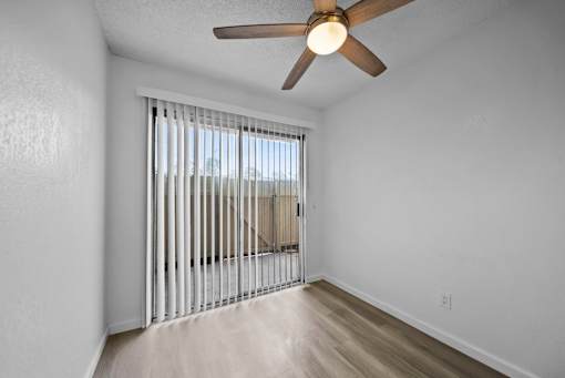 A room with a ceiling fan and sliding glass doors.
