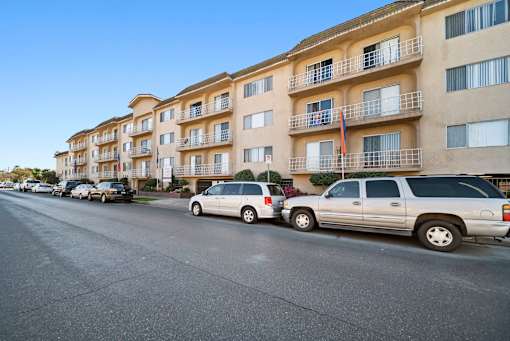 A row of apartment buildings with cars parked in front.