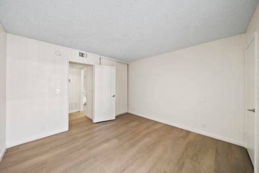 A room with white walls and wood flooring with a doorway leading to another room.