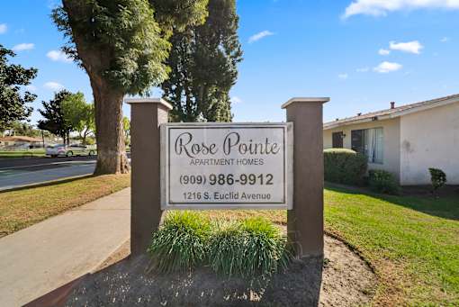 A sign for Rose Pointe Apartment Homes stands in front of a tree.