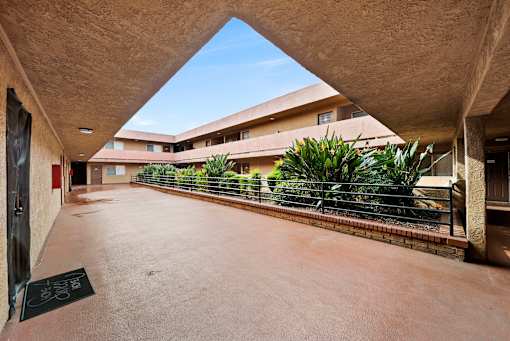 A courtyard with a triangular roof and a fence with plants on it.