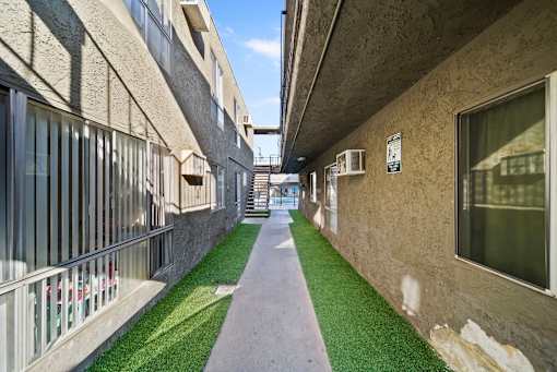 A long, narrow walkway between two buildings with grass on the ground.