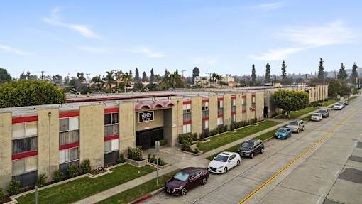 A long building with a red awning sits on a street with cars parked in front.