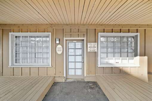 A wooden porch with a door and windows.