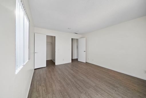 A room with white walls and wooden flooring with three doors.