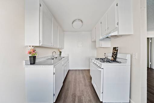 A white kitchen with a sink, stove, and cabinets.