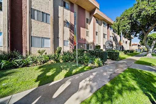 A concrete pathway leads through a grassy area in front of apartment buildings.