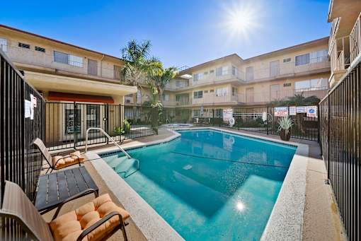 A sunny day at a poolside with chairs and apartment buildings in the background.