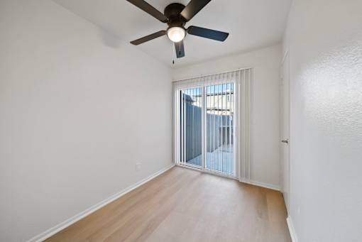 A room with a ceiling fan and sliding glass doors.