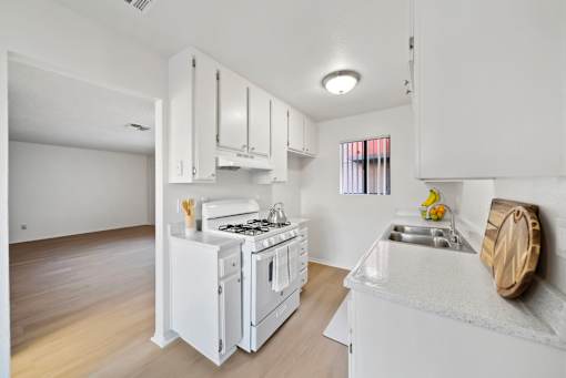 A white kitchen with a stove, sink, and cabinets.