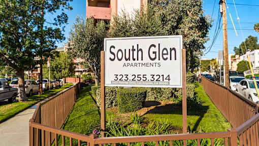 A sign for South Glen Apartments is displayed in front of a fence.