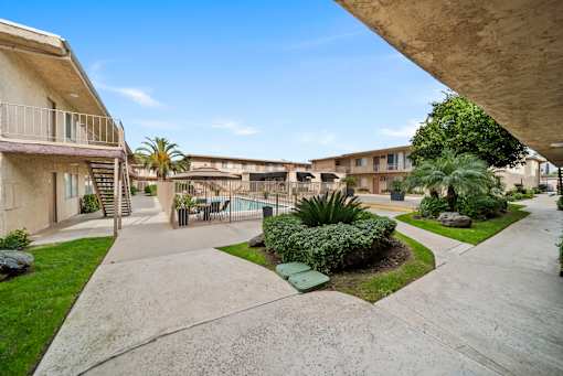 A concrete walkway leads to a pool surrounded by apartment buildings.