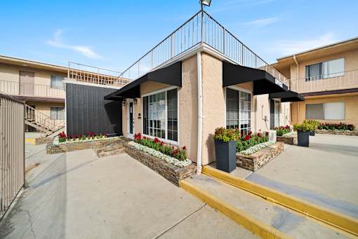 A modern house with a black awning and a stone wall with red flowers in front.