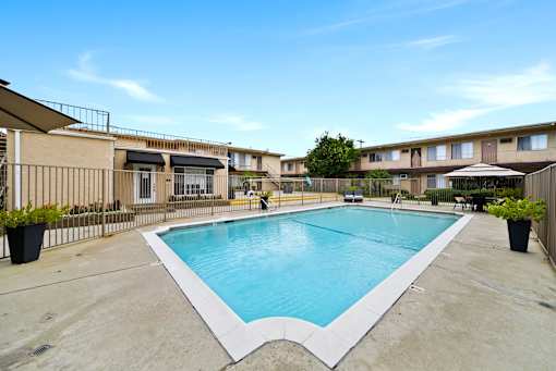 A large outdoor swimming pool surrounded by a fence and apartment buildings.