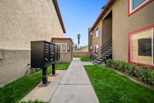 A black mailbox is on the left side of a sidewalk in front of a tan building.