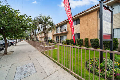 A red banner with white text hangs on a black pole in front of a building.