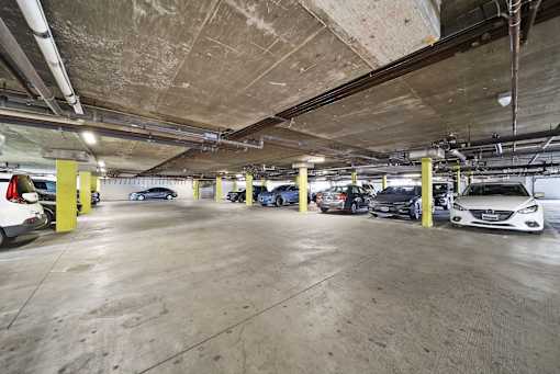 A parking garage with several cars parked and yellow poles.