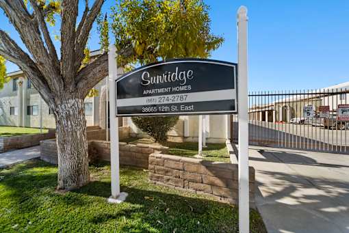 A sign for Sunridge Apartment Homes stands in front of a tree.