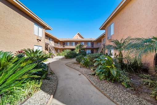 A pathway leads through a landscaped courtyard between two tan buildings.