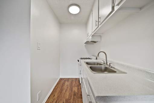A small, white kitchen with a sink and a wood floor.